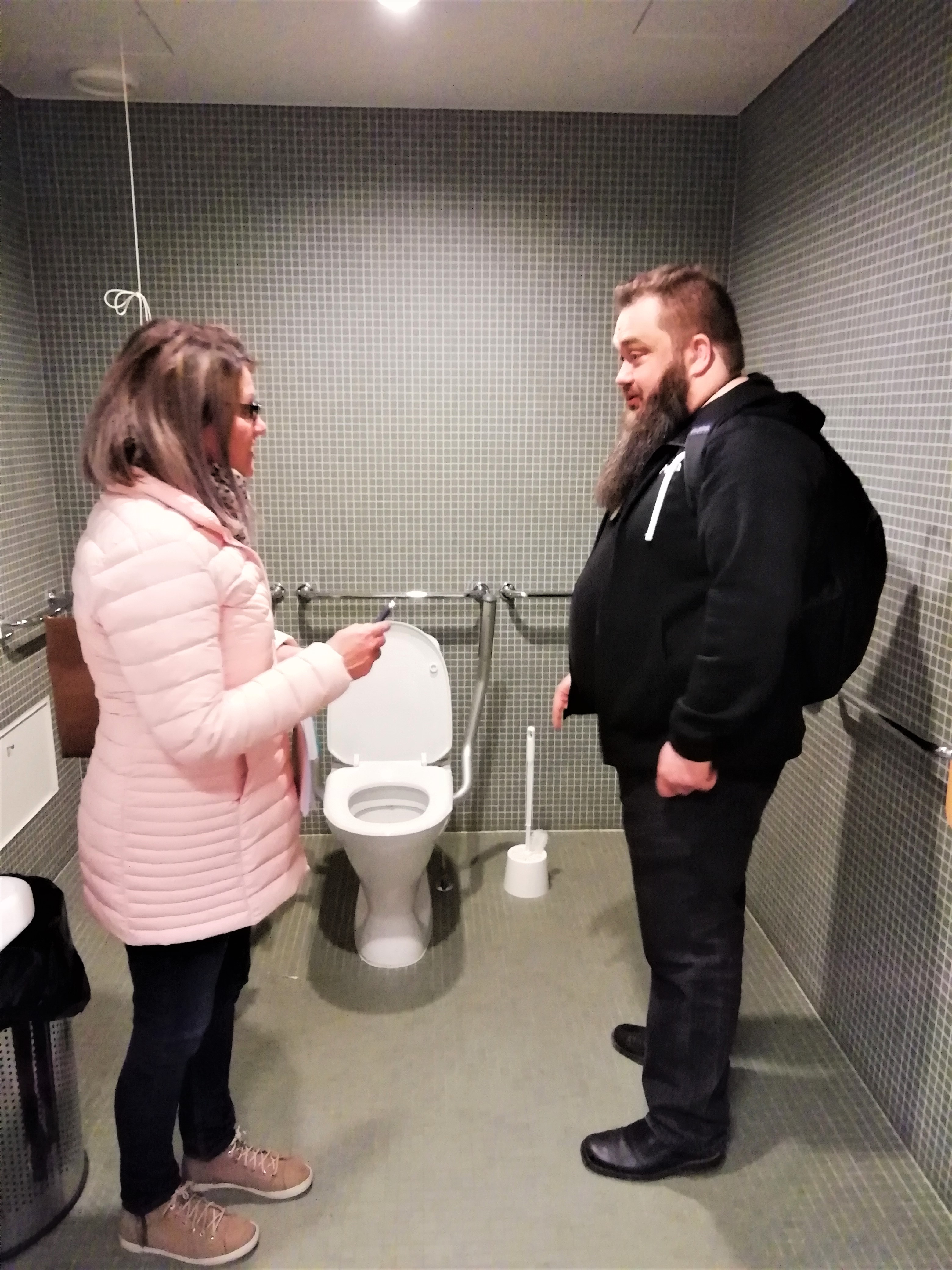 Tarja Räsänen ja Peeta Piiparinen seisovat inva-WC-tiloissa ja keskustelevat.